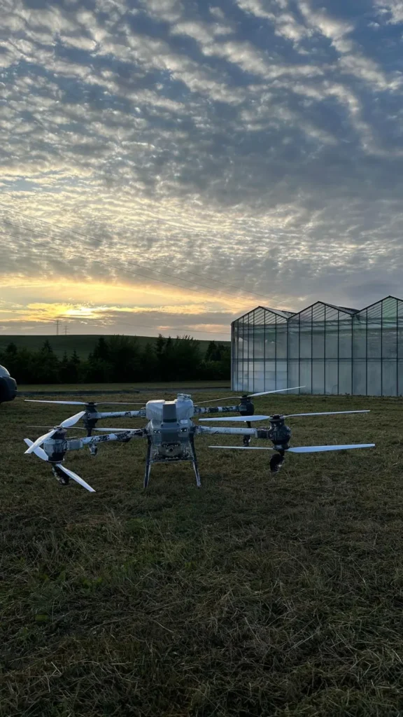 Dron Agras T50 na łące przy szklarniach